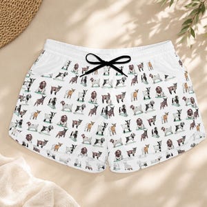 Könnte beinhalten: Weiße Sporthose mit schwarzem Kordelzug und einem sich wiederholenden Muster verschiedener Hunderassen in Braun, Schwarz und Weiß. Die Shorts haben eine lockere Passform und sind aus leichtem Material gefertigt.