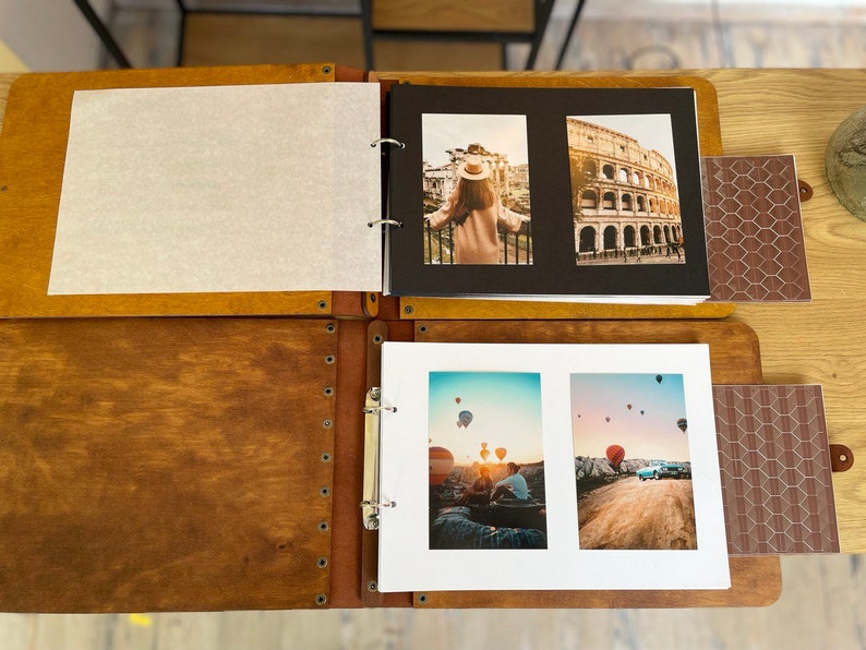 K&ouml;nnte beinhalten: Ein braunes Lederfotoalbum mit einer wei&szlig;en Seite, einer schwarzen Seite mit einem Foto einer Frau mit Hut, die vor dem Kolosseum in Rom steht, und einer wei&szlig;en Seite mit zwei Fotos von Hei&szlig;luftballons in Kappadokien, T&uuml;rkei.