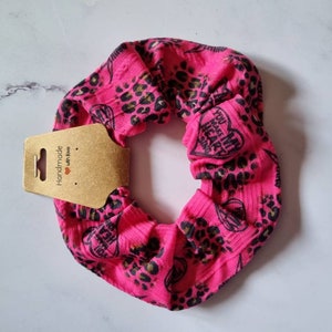 May include: Pink scrunchie with a leopard print and the text "You make my heart sing" in black.