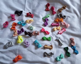 May include: A collection of colorful hair bows in various colors and styles, including pink, blue, green, yellow, orange, and purple. The bows are made of fabric and have a variety of different shapes and sizes.