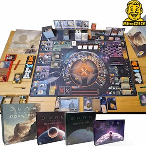 Puede incluir: Una configuración de juego de mesa con un tablero de juego grande y detallado, cartas, fichas y piezas de juego. Se ven cuatro cajas de juego, cada una con la palabra "Dune". El juego está sobre una mesa de madera marrón claro.
