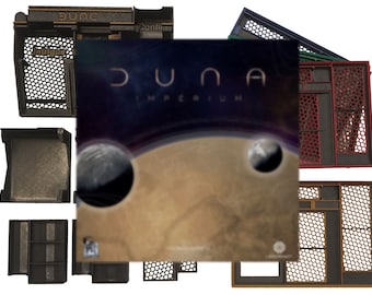May include: The board game "Dune: Imperium" is displayed with various game components. The box art features a planetary landscape and the game's title. Several game component trays and dividers are also visible, in shades of brown, black, and red.