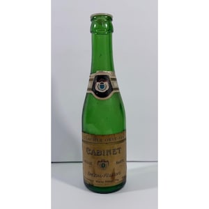 May include: A green glass bottle with a label that reads "Cabinet Spezial-Füllung". The bottle has a long neck and a small, round base. The label is brown and gold with black text and a crest.