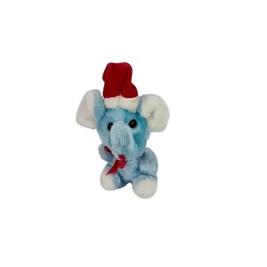 May include: A plush blue elephant toy with white ears and feet, wearing a red Santa hat and a red bow. The stuffed animal is designed for the holiday season.