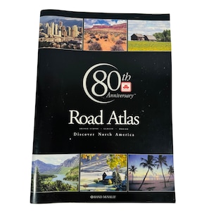 以下が含まれることがあります： 「80th Anniversary」と「Road Atlas」のテキストと「Discover North America」のタグラインが書かれた黒と赤の表紙。表紙には、都市の風景、砂漠の風景、農家、山、森、ビーチの画像が掲載されています。
