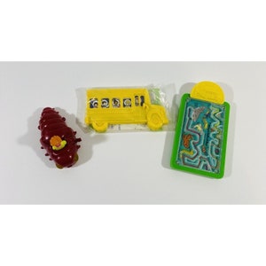 May include: A set of three plastic toys: a yellow school bus with a smiling driver and passengers, a red and brown caterpillar with a yellow head, and a green plastic clipboard with a maze and sea creatures.