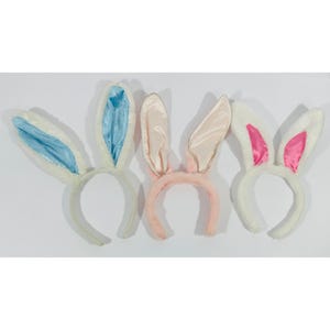 May include: Three Easter bunny ear headbands. One has white fur with blue satin lining, another has pink fur with pink satin lining, and the last has white fur with pink satin lining. The headbands are made of soft, plush material.