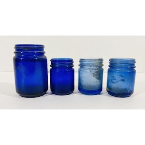 May include: Four cobalt blue glass jars of varying sizes. The jars are all round and have a smooth, shiny surface.