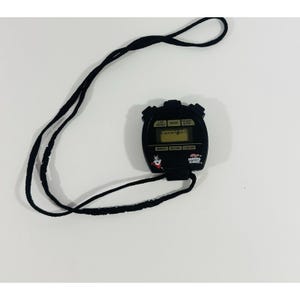 Op de afbeelding: Zwarte digitale stopwatch met een zwart koord. De stopwatch heeft een wit display met de woorden "LAP RESET", "MODE", "START STOP", "MINUTE", "SECOND", en "1/100 SEC". De stopwatch heeft een cartoon afbeelding van Tony de Tiger van Frosted Flakes ontbijtgranen.