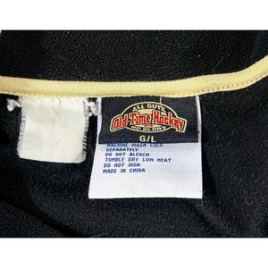 Puede incluir: Chaqueta de forro polar negra con ribete color crema y una etiqueta que dice "Old Time Hockey". La etiqueta tambi&eacute;n incluye instrucciones de lavado. La chaqueta es talla G/L.