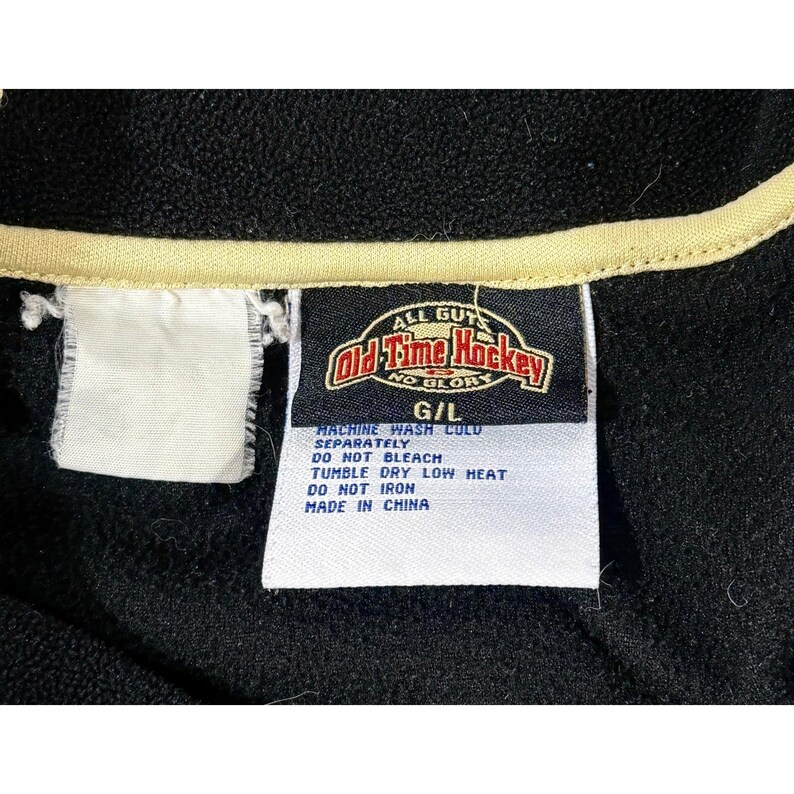 Puede incluir: Chaqueta de forro polar negra con ribete color crema y una etiqueta que dice "Old Time Hockey". La etiqueta tambi&eacute;n incluye instrucciones de lavado. La chaqueta es talla G/L.