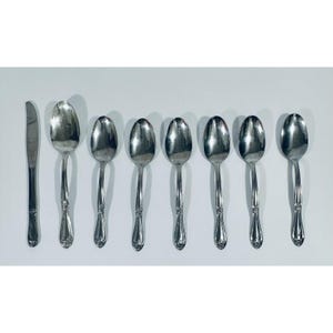 May include: A collection of silver-colored silverware, including a knife and several spoons. The spoons have a classic design with a decorative pattern on the handle. The silverware is arranged on a white surface.
