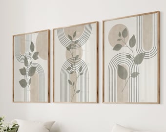 May include: Three abstract art prints with a minimalist design featuring green leaves and brown arches. The prints are framed in natural wood and hung on a white wall above a beige sofa.