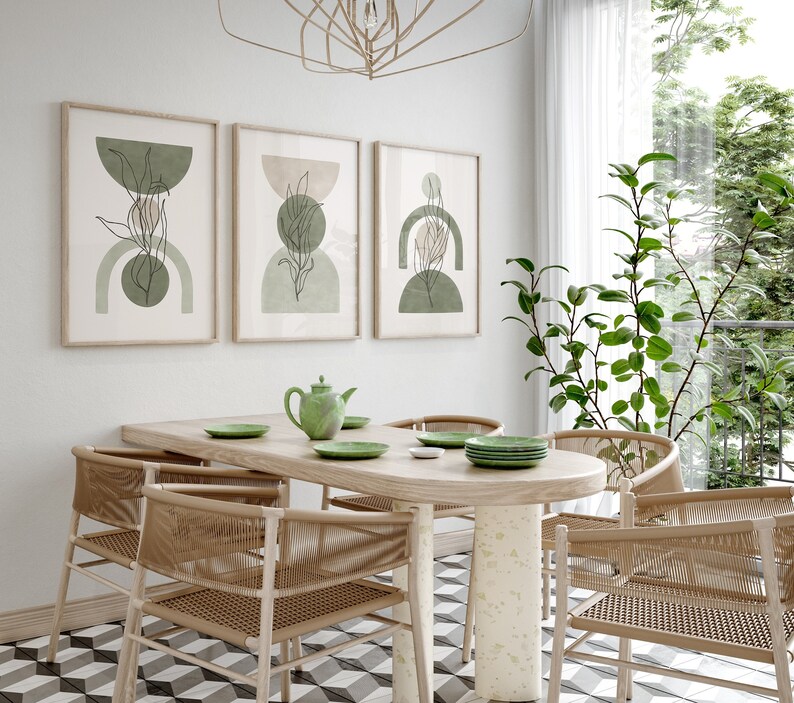May include: A dining room with a wooden table and six woven chairs. The table has a green teapot and green plates on it. Three framed prints with green and brown abstract designs hang on the wall behind the table.