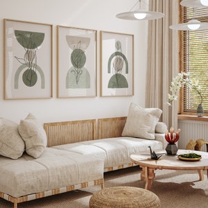 May include: A light beige sectional sofa with three cushions and a wooden frame. The sofa is in a living room with three framed abstract art prints with green and brown geometric shapes. A small round wooden coffee table with a black origami crane and a vase of red flowers sits in front of the sofa.
