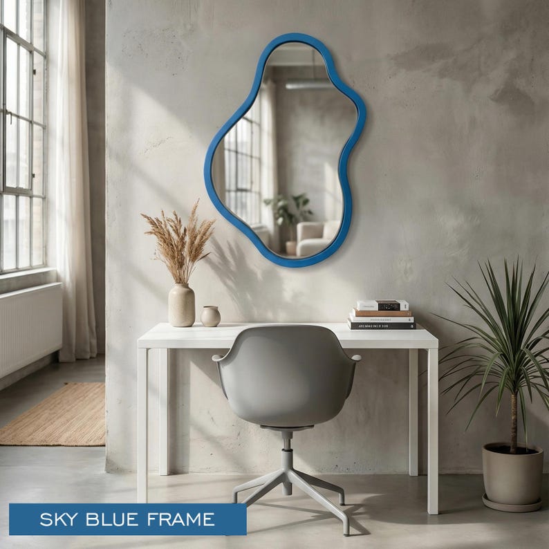 May include: A wall-mounted mirror with an irregular, organic-shaped sky blue frame. The mirror features a reflective glass surface and is positioned above a white desk. The text "SKY BLUE FRAME" is visible in the lower left corner.