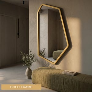 Peut inclure: Un miroir mural doté d'une forme géométrique irrégulière et asymétrique avec un cadre doré lisse. La surface réfléchissante offre une vue claire de l'espace intérieur, capturant la lumière et les ombres sur les bords du cadre métallique.