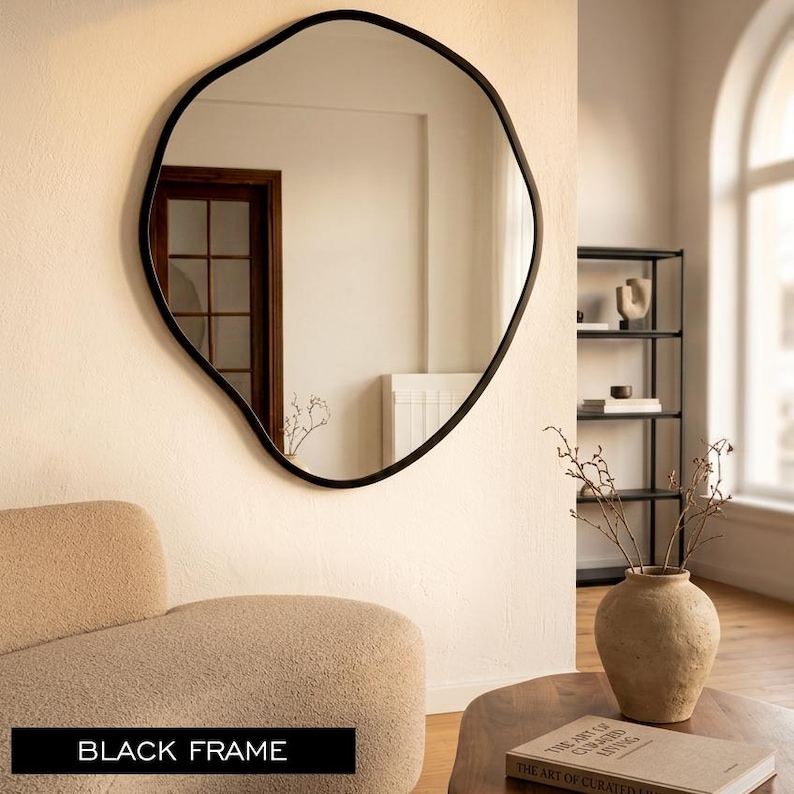 Peut inclure: Un miroir mural dot&eacute; d'un cadre noir aux formes irr&eacute;guli&egrave;res et organiques. La surface r&eacute;fl&eacute;chissante montre l'int&eacute;rieur d'une pi&egrave;ce avec une porte et des murs clairs. Le miroir pr&eacute;sente un bord noir lisse et continu autour du verre.