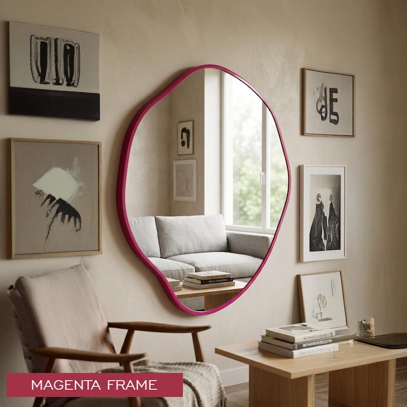 Peut inclure: Un grand miroir mural de forme organique irr&eacute;guli&egrave;re dot&eacute; d'un cadre magenta vif. La surface r&eacute;fl&eacute;chissante montre une vue claire de l'int&eacute;rieur d'une pi&egrave;ce, incluant un canap&eacute; et une fen&ecirc;tre, avec le texte MAGENTA FRAME en bas.