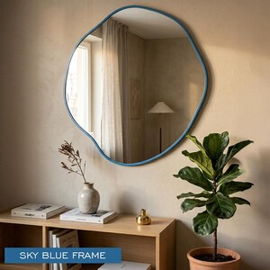 Peut inclure: Un miroir mural de forme organique irr&eacute;guli&egrave;re dot&eacute; d'un cadre bleu ciel lisse. La surface r&eacute;fl&eacute;chissante offre une vue claire d'un espace int&eacute;rieur, capturant la lumi&egrave;re et les environs dans son design de bordure unique et asym&eacute;trique.