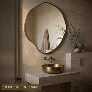 Peut inclure: Un miroir mural organique et asym&eacute;trique dot&eacute; d'un fin cadre vert olive. Le miroir refl&egrave;te l'int&eacute;rieur d'une salle de bain avec une serviette et une petite bouteille. Le design est irr&eacute;gulier et fluide, offrant un contraste avec le mur.