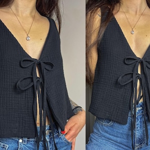 May include: A black sleeveless top with a tie-front detail. The top is made of a soft, textured fabric and has a relaxed fit.