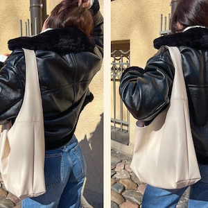 Pode incluir: Uma jaqueta de couro preta com gola de pele sintética e uma grande bolsa tote de cor bege.