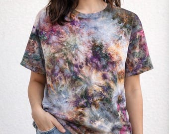 May include: A short-sleeved t-shirt with a tie-dye pattern in shades of purple, pink, green, and brown. The shirt is made of soft material and is paired with blue jeans. The tie-dye design creates a unique, artistic look.