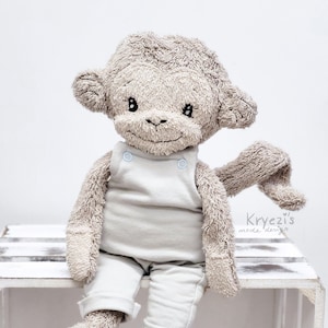 May include: A plush monkey toy wearing a light blue jumpsuit with a white trim. The monkey is sitting on a white wooden crate.