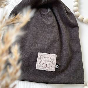May include: A dark gray beanie with a pink fox embroidered patch and a small black tag that says "HEY".