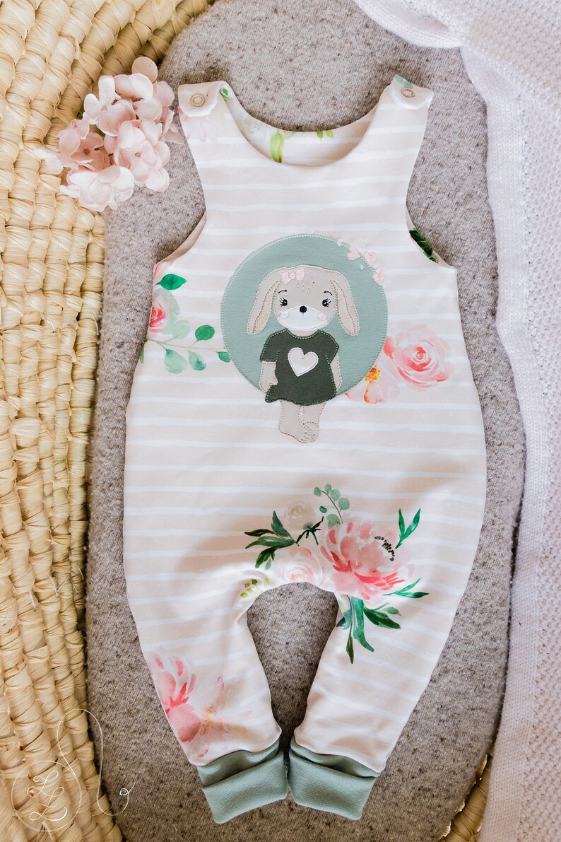 May include: White and green striped baby overalls with a floral print and a green and brown applique of a bunny with a heart on its shirt.
