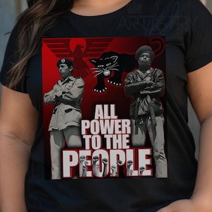 May include: Black t-shirt featuring a graphic design with the text "ALL POWER TO THE PEOPLE." The design includes images of two figures, a black panther, and an eagle against a red background. The shirt is a crew neck.