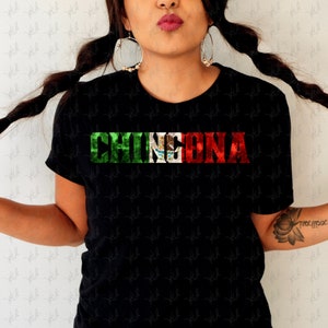 May include: Black t-shirt with the word "CHINGONA" printed in white letters with a distressed look. The letters are layered with the colors of the Mexican flag: green, white, and red.