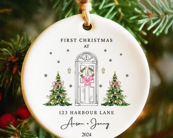 May include: White ceramic Christmas ornament with a black and white illustration of a house with a wreath on the door. The ornament also has the text "First Christmas at 123 Harbour Lane Anson + Jenny 2024".