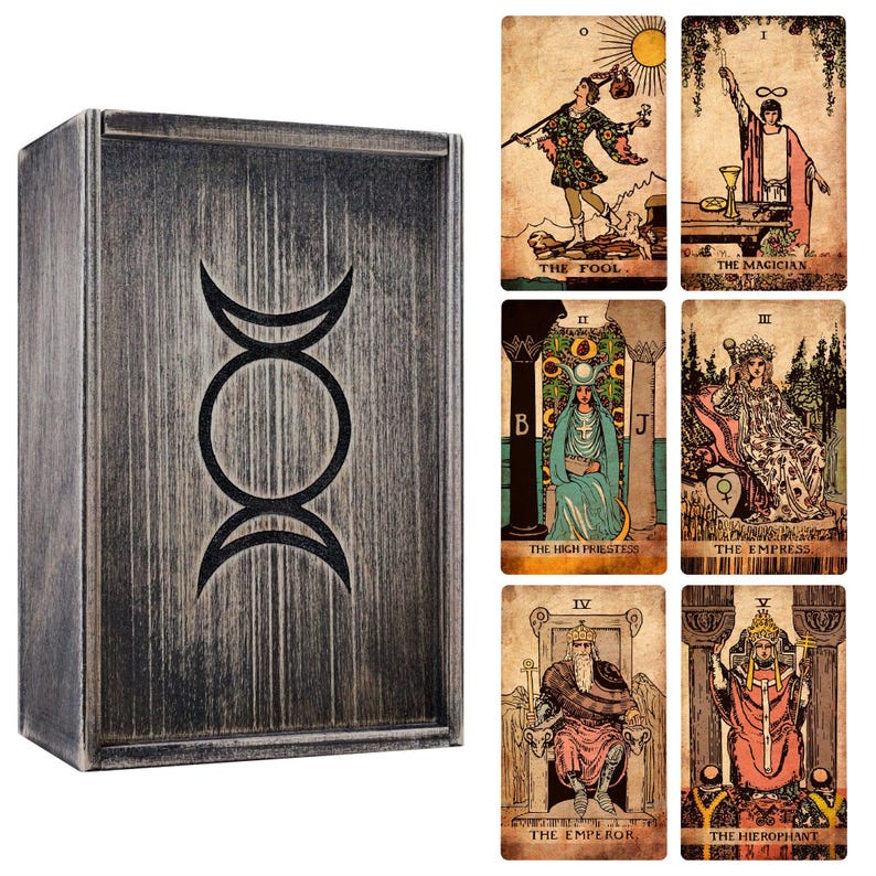 May include: A wooden tarot card box with a silver finish and a black triple moon symbol. The box is displayed with several tarot cards featuring illustrations and titles such as "The Fool" and "The Magician."