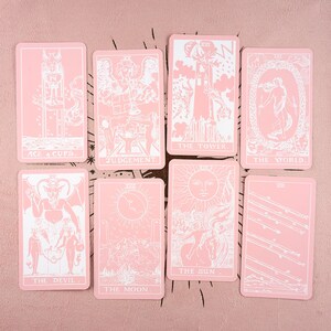 May include: A set of eight tarot cards with a pink background. Each card features white illustrations and text, including "Ace of Cups," "Judgement," "The Tower," "The World," "The Devil," "The Moon," and "The Sun."