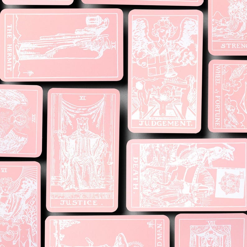 May include: A collection of pink tarot cards with white illustrations and text. The cards feature various designs, including figures, symbols, and the words "JUDGEMENT" and "JUSTICE". The cards are arranged on a black surface.