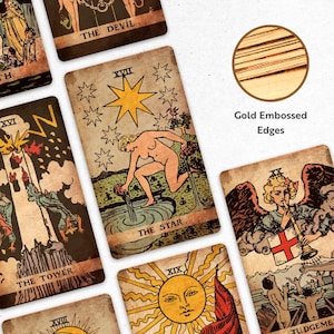 May include: A collection of vintage-style tarot cards with gold embossed edges. The cards feature illustrations and text, including "THE STAR," "THE DEVIL," and "THE TOWER." The artwork has a distressed, aged appearance.