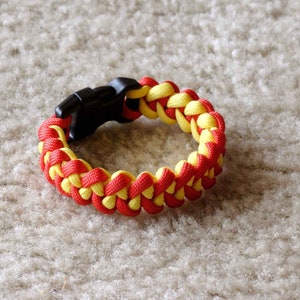 May include: A red and yellow paracord bracelet with a black plastic clasp.