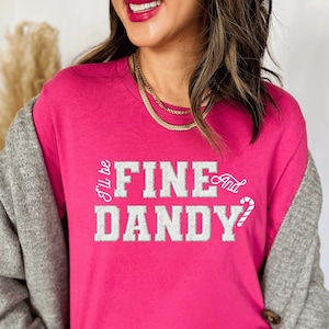 Könnte beinhalten: Ein pinkfarbenes T-Shirt mit einer weißen Grafik, auf der "I'll be fine and dandy" mit einem Zuckerstangen-Motiv steht.
