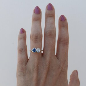 May include: A gold ring with a blue triangular gemstone and a clear rectangular gemstone.