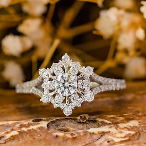 May include: A silver snowflake engagement ring with a large round center stone and smaller stones surrounding it.
