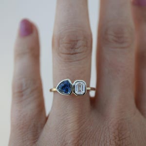 May include: A gold ring with a blue triangular gemstone and a clear rectangular gemstone.