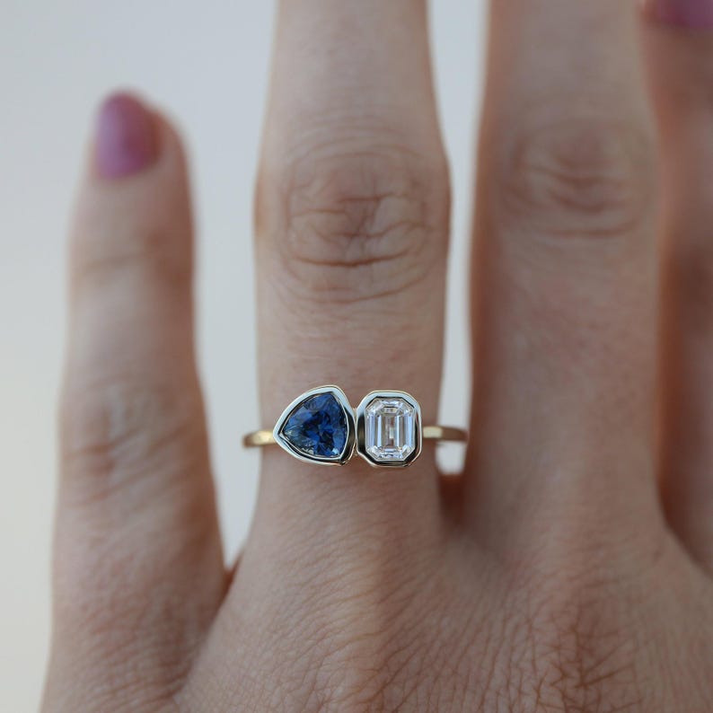 May include: A gold ring with a blue triangular gemstone and a clear rectangular gemstone.