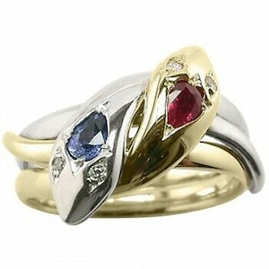 May include: A gold, silver, and white snake ring with a red ruby and blue sapphire gemstone. The ring is set with diamonds.