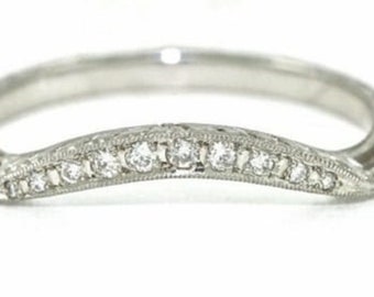 May include: A delicate, curved wedding band with a row of small diamonds set in a platinum or white gold band. The band features intricate, engraved details.