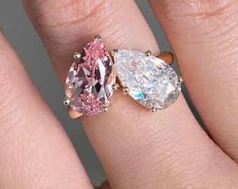 May include: A gold ring featuring two pear-shaped gemstones. One is a light pink color, and the other is clear. The gemstones are set with small gold prongs.