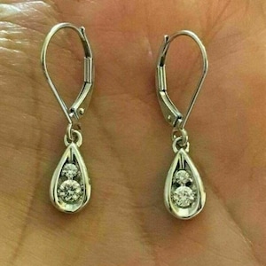 May include: A pair of silver dangle earrings with a teardrop-shaped pendant featuring two clear round gemstones.