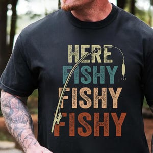 May include: A black t-shirt with a vintage-style graphic that says "Here Fishy Fishy Fishy" with a fishing rod and lure.