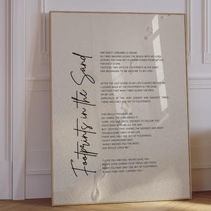 以下が含まれることがあります： 左側に大きな黒い筆記体で「Footprints in the Sand」という文字が書かれ、薄いベージュの背景に淡い足跡の模様と、小さな黒い文字で詩の全文が印刷された長方形のウォールアートプリント。